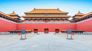 Frontansicht der Verbotenen Stadt in Peking mit roten Mauern, goldenen Dächern und einem breiten Platz davor.