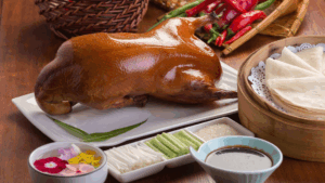 Gebratene Peking-Ente mit Pfannkuchen, Gurken, Lauch, Sauce und Beilagen auf einem Tisch.