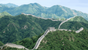 Die Große Mauer von China windet sich durch grüne Berge mit Wachtürmen und befestigten Abschnitten.