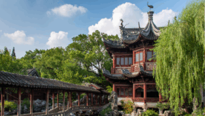 Traditionelles Holzgebäude im Yu-Garten in Shanghai mit geschwungenen Dächern, Bäumen und überdachtem Gang.