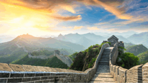 Die Große Mauer von China bei Sonnenaufgang, mit Wachtürmen und Berglandschaft im Hintergrund.