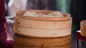 Frisch gedämpfte chinesische Dumplings in einem runden Bambusdämpfer, aus denen Dampf aufsteigt.